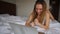 Jocund girl winning bet online by laptop and lying in white quilt at hotel.