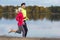 Jogging Concepts. Running Couple While Training Outdoors on Road At River For Durable Marathon Pretty Young Female and Extremely