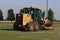 John Deere road grader in a field with green grass and blue sky in Kansas.