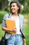 Jolly carefree girl embracing books in park while coming home after classes in university. Cheerful attractive young woman looking