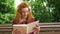 Jovial red haired girl laughing at funny book in park