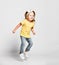 Joyful active kid baby girl blonde with handband in yellow t-shirt and blue jeans is jumping high, having fun, skipping