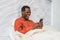 Joyful African-American man holds smartphone lying in bed