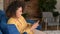 Joyful African-American woman using smartphone sitting on the comfortable sofa at home