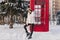 Joyful amazing girl in warm winter clothes enjoying winter morning near red telephone box. Attractive young woman on