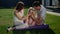 Joyful american dream family are sitting outdoors on the lawn near the house on a purple blanket, carpet or rug. Parents