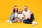 Joyful Arabic Family Wearing Santa Hats Sitting Over Yellow Background