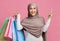 Joyful arabic woman in hijab holding smarphone and bright shopping bags