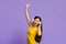 Joyful asian girl in wireless headphones dancing and singing over purple background