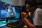 Joyful asian teen gamer man playing video games on computer in d