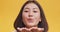 Joyful asian woman sending blow kiss to camera, flirting over orange studio background, close up portrait