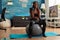 Joyful athletic black person in leggings sportwear using stability ball for training