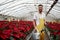 Joyful atmosphere. Portrait of beautiful young guy in the hothouse taking care of flowers