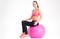 Joyful attractive young sportswoman sitting on pink fitball