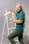 Joyful bearded foreman in green t-shirt with brush roller and ladder