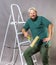 Joyful bearded foreman in green t-shirt with brush roller and ladder