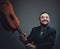 Joyful bearded man holding guitar psoes in dark background alone