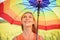 Joyful beautiful girl holding multicolored umbrella in sunflower field and blue cloud sky background