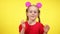 Joyful beautiful little girl with glowing toy mouse ears on head dancing at yellow background. Portrait of cheerful