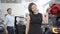 Joyful beautiful woman posing with car keys in dealership as blurred young man opening vehicle door at the background