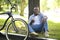 Joyful black biker sitting near tree with mobile phone at urban park