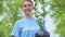 Joyful blond woman holding tree sapling smiling on camera in park, eco volunteer
