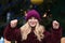 Joyful blonde woman dressed in red knitted hat and warm coat holding glowing sparklers at the Christmas tree