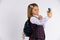 Joyful blondine schoolgirl taking selfie on mobile phone and gesturing hello sign on white background with free space