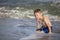 Joyful boy near the sea plays with the waves.