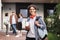 Joyful boy with red headphones standing with backpack and books in hand and happily looking in camera in courtyard of