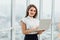 Joyful business woman standin in office, holding laptop.