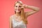 Joyful carefree attractive confident blond woman in stylish silver dress show disco sign victory peace gesture near eye