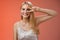 Joyful carefree attractive confident blond woman in stylish silver dress show disco sign victory peace gesture near eye