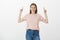 Joyful and carefree beautiful woman in casual outfit, raising hands and pointing up with index fingers, smiling broadly