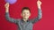 Joyful caucasian boy 7-8 years old with a balloon rejoices and raises his hands up. Studio shooting, red background. The child rej