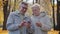 Joyful caucasian elderly couple walking in autumn park hold smartphone use mobile internet browser read good news watch