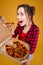 Joyful charming young woman standing and tasting pizza