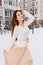 Joyful charming young woman in white woolen sweater and light beige skirt enjoying cold winter weather. Time of snow