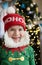 joyful child, 7-year-old boy in elf costume, Santa hat against of bokeh from garlands