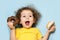 Joyful child screams with happiness. emotional girl eating tasty donuts with chocolate and white icing. trend in food, sweets for