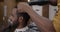 Joyful client smiling while barber brushing and drying his hair with electric dryer in barbershop