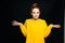 Joyful confused young woman wearing yellow sweater shrugging shoulders on isolated black background