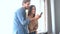 Joyful couple looking mobile phone at home. Smiling husband hug wife near window