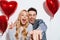 Joyful couple pointing finger at camera while posing with heart balloons