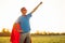 Joyful courageous man in a superhero costume poses on the field against the backdrop of sunset