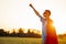 Joyful courageous man in a superhero costume poses on the field against the backdrop of sunset