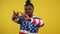 Joyful dance of happy African American man at yellow background. Positive cheerful guy in hoodie with USA flag print