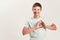 Joyful disabled boy with Down syndrome smiling at camera, making heart shape with his hands while standing isolated over