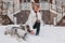 Joyful fashionable young woman having fun with husky dog in snow on street outdoor. Love domestic pets, lovely moments