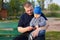 Joyful father sitting with his displeased son on a bench in the park